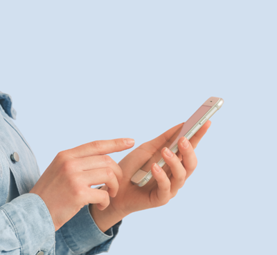 Hands holding a smartphone while tapping and swiping the screen, with a denim sleeve visible against a plain blue background.